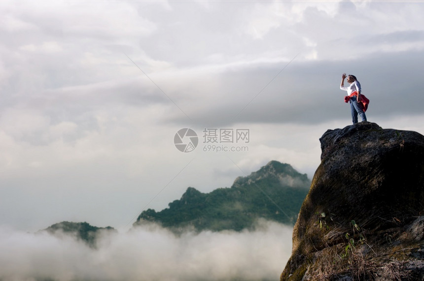勇气亚洲女登山者或背包站立透过日落时岩石峰顶的高树仰望着亚洲女登山者或背负式妇女领导成功图片