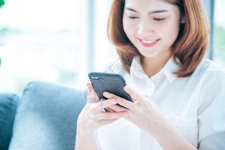 亚裔女使用智能手机阅读网络社交媒体购物网站在Smartphone上微笑脸的智能手机网站上使用智能手机阅读线上社交媒体拥有手机检查背景图片