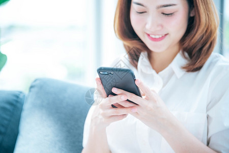 视频博客亚裔女使用智能手机阅读网络社交媒体购物网站在Smartphone上微笑脸的智能手机网站上使用智能手机阅读线上社交媒体拥有背景图片
