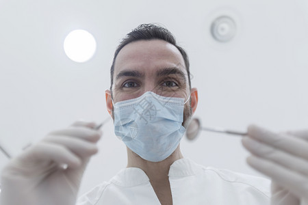 戴外科口罩的牙医手持钻孔工具图片
