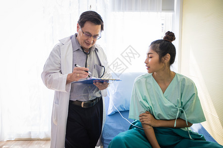 外科医生向躺在院床上的一位女病人询问和解释情该名女人在医院卧床生病的访问背景图片