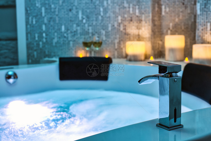 室内的水疗按摩浴缸特写水龙头中的蓝色冒泡水背景上装饰着蜡烛放松和生活方式抽象背景蓝色灯光美丽水疗按摩浴缸特写水龙头中的蓝色冒泡水图片