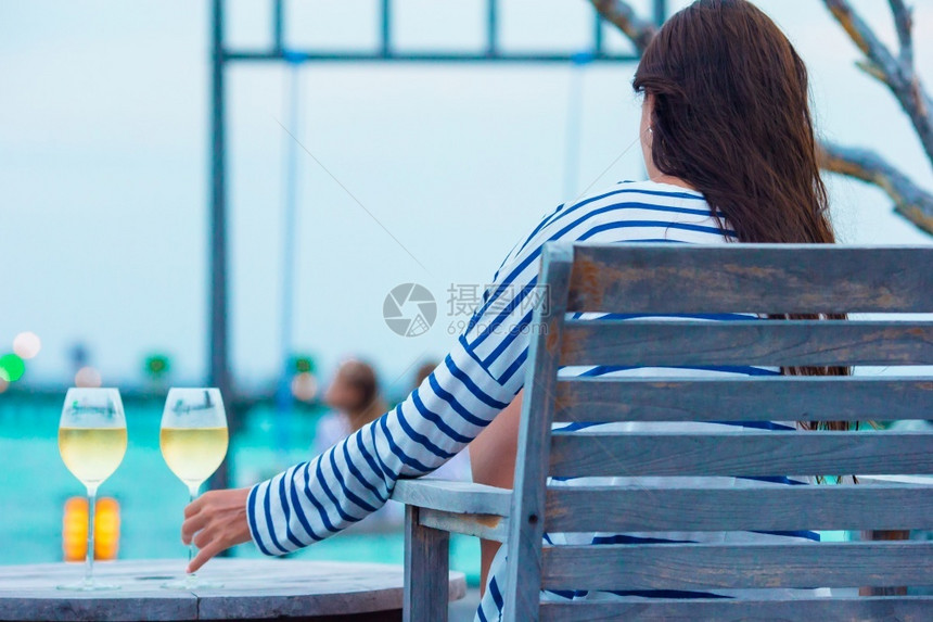 女孩夏天采取马尔代夫日落时喝一杯白葡萄酒的年轻女子晚上喝一杯白葡萄酒的年轻女子图片