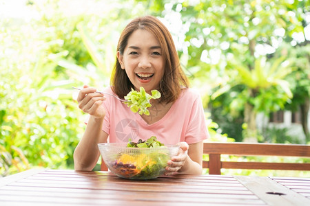 女坐在花园旁边房子阳台上吃健康绿色沙拉的保健和营养食品概念她认为在家庭园圃旁边的露台里生活着一个健康的绿色沙拉一种重量高清图片