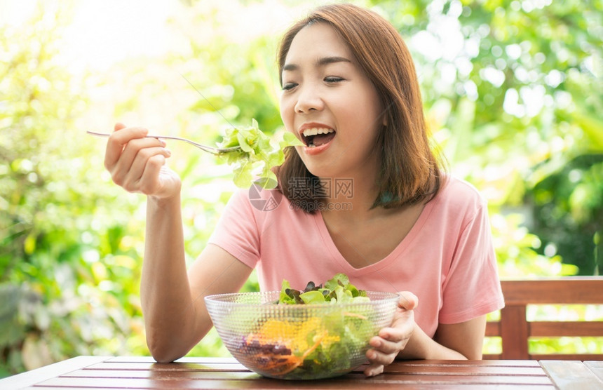节食吸引人的坐在花园旁边房子阳台上吃健康绿色沙拉的保健和营养食品概念她认为在家庭园圃旁边的露台里生活着一个健康的绿色沙拉饮食图片