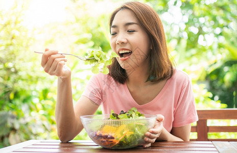 节食吸引人的坐在花园旁边房子阳台上吃健康绿色沙拉的保健和营养食品概念她认为在家庭园圃旁边的露台里生活着一个健康的绿色沙拉饮食高清图片