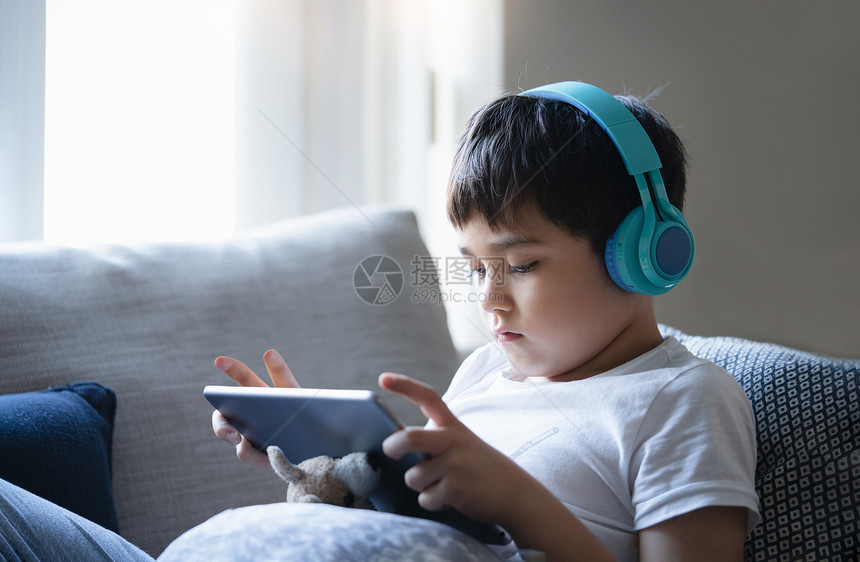 学前班卡通片坐在沙发上的小孩在石板上看漫画可爱男孩坐在窗边跟朋友网上玩游戏线的图片