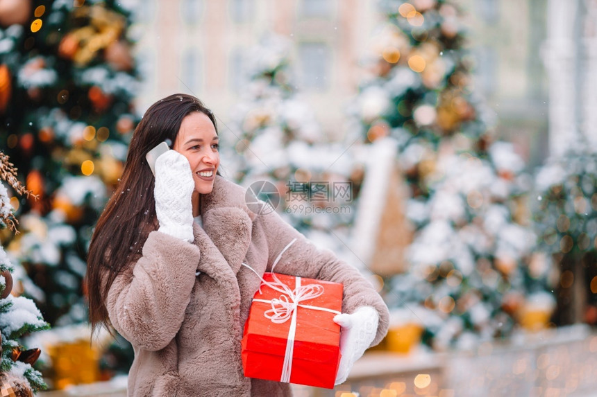 Beautidul女孩圣诞节有红礼物与智能手机在雪户外的屋欢乐女孩镇地标城市图片