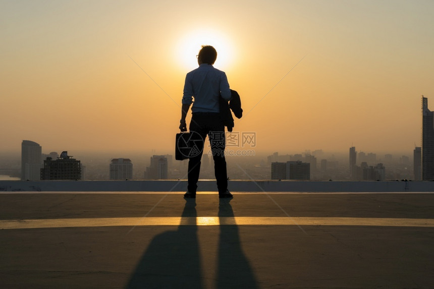 包金融天际线年轻商人穿着舒适的便衣外套站在大楼顶上拿着一个工作袋仰望高的现代建筑城市景天线视野商业务等概念构想城市观光图片
