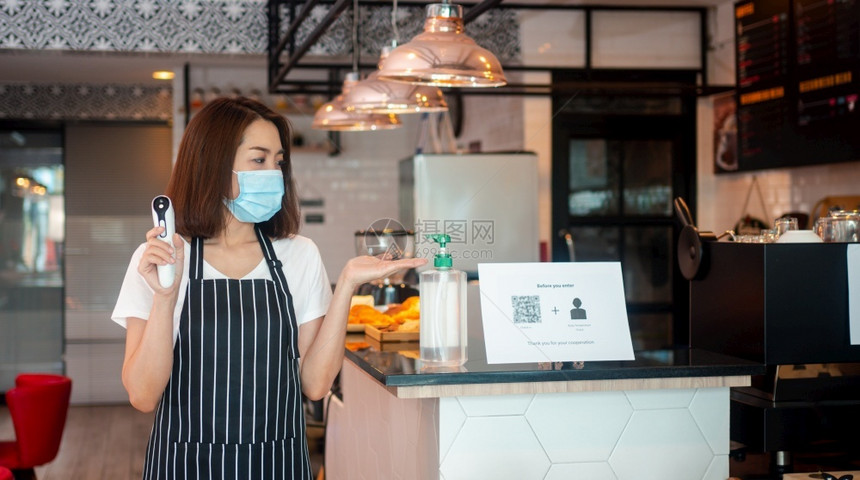 商业查看女身戴面罩和持有红外前额温度计的亚洲女服务员在进入餐馆咖啡店之前检查顾客身上的症状以检查体温在进入餐厅咖啡店之前检查客户图片