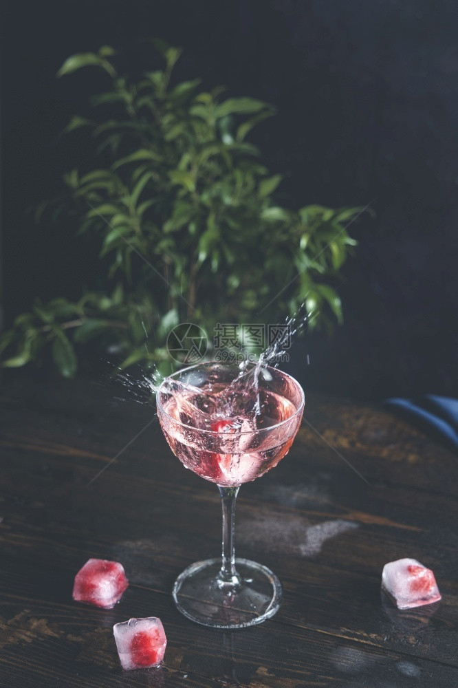 香槟酒鸡尾粉红玫瑰香槟在优美玻璃中盛溢冰冻的草莓在深黑木板桌面的冰块上紧闭浅的田地深处气泡图片