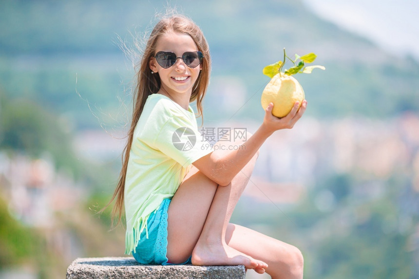 意大利语象征阿马尔菲海岸背景的小女孩在地中海和天空背景中手握着大黄柠檬在海洋和天空背景下旅游的图片