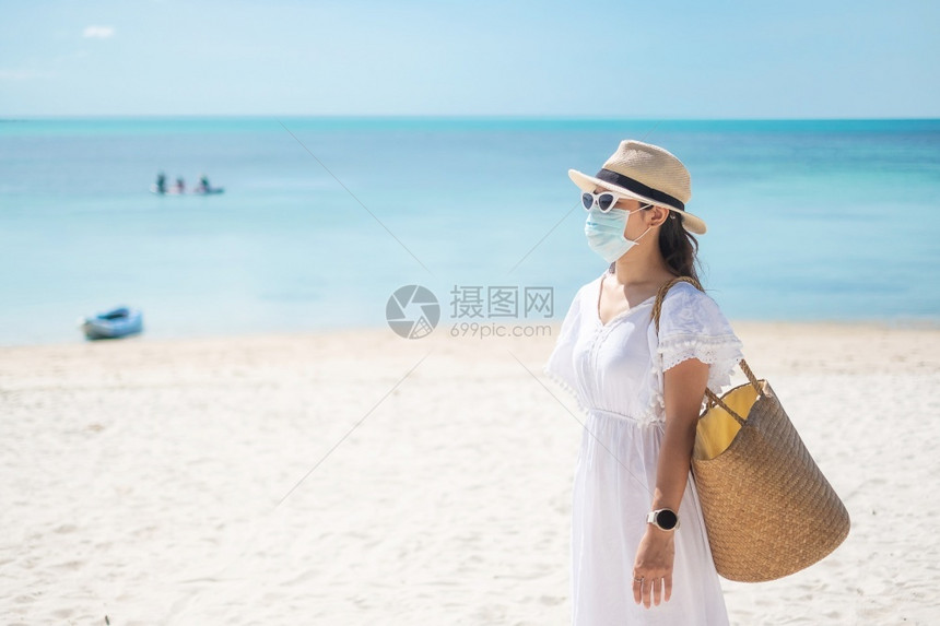 普通的身戴外科面罩快乐旅游妇女在热带海滩保护处享受美丽的海沙和白Corona疾Covid19感染新常态旅行假期和日人们放松图片