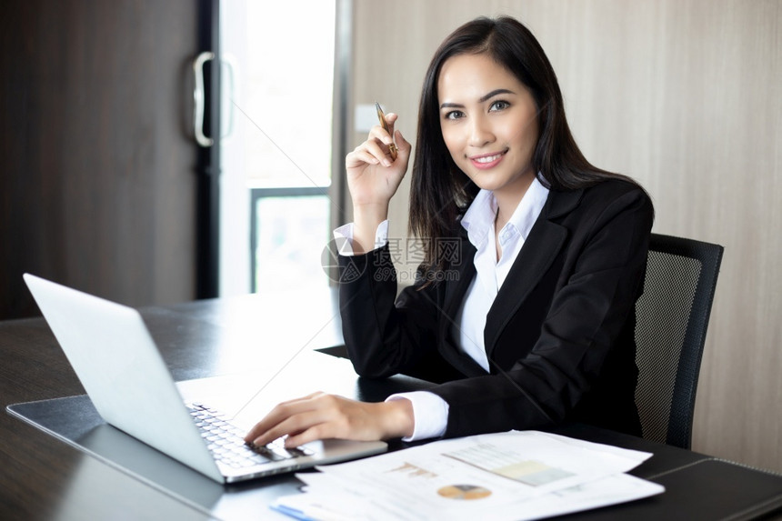 互联网管理女士亚洲企业家在办公桌上持有笔和分析文件的亚洲女企业家手持膝上型计算机和图表财务并在背景中工作与亚洲女商人一起使用笔纸图片