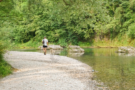 荒野中一个带着帽子的年轻人和狗在河边散步图片