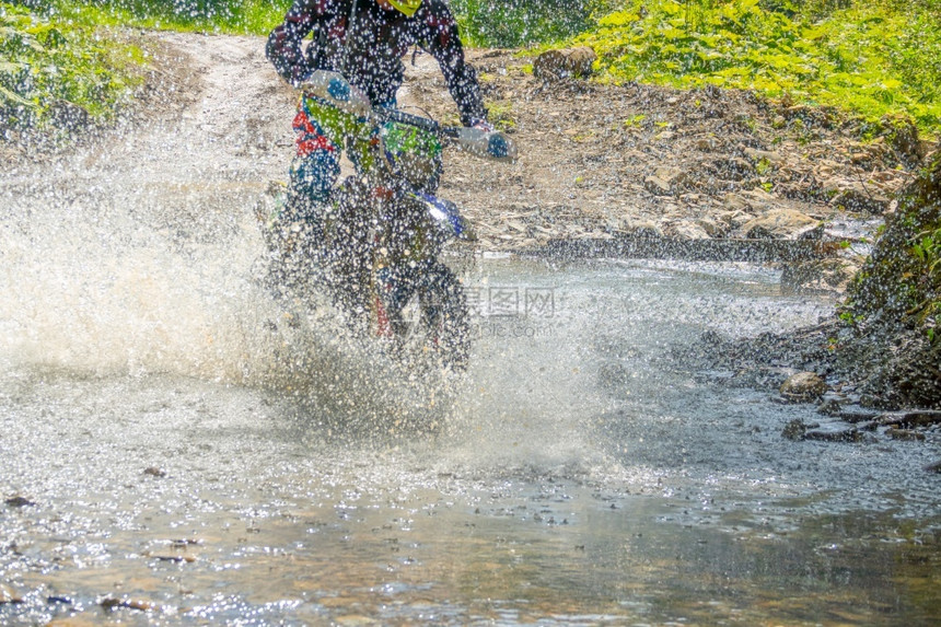 种族阳光夏日的白天和森林树木大量水喷洒隐藏着一辆内置摩托车在水喷雾中无法辨认出艾特利Enduro夏天湿的图片