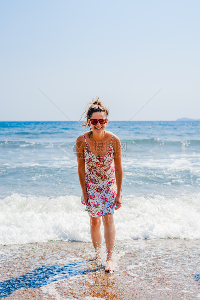景观休息海洋在度假旅行期的海边滩上站在边看着摄影机笑镜头时身穿夏衣的年轻女子背后视线图片