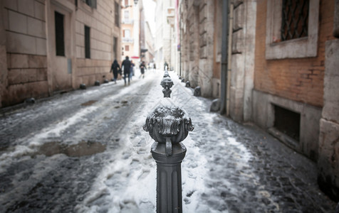 被雪装饰建筑近距离观看一个装饰着交通覆盖的圆柱子在城市小巷中被雪封在一栋城胡同里人们在幕后行走外部的过去城市背景
