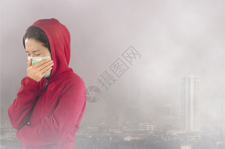 烟雾脸素材脸遭受妇女有流感喷嚏妇女穿着粉红色的冬季衣着戴面罩在她的鼻子上面对曼谷市覆盖有毒尘埃的感寒冷和流健康概念身穿针粉色的冬季衣服对曼背景