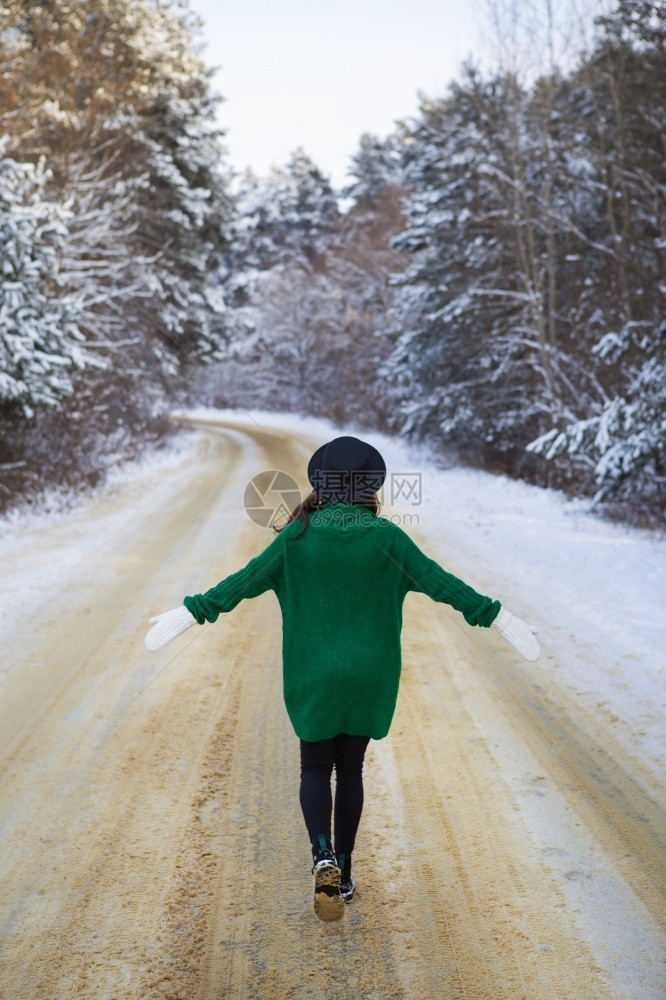 户外覆盖有雾一个穿着绿色毛衣和帽子的年轻女孩在茂密的松林中走在雪路间图片