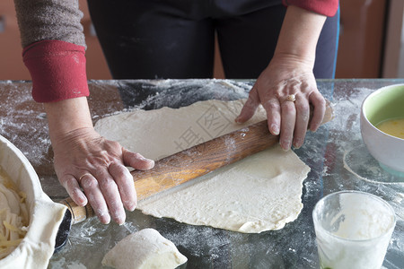 女人双手在玻璃桌上卷着面团做蛋糕干芝士面包馅饼加卷心菜甜点美味的糕图片