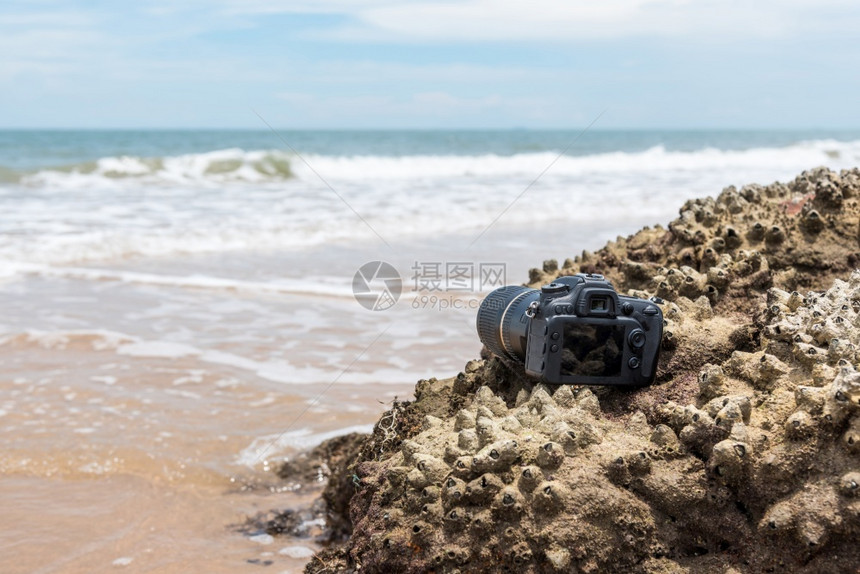 现代的在极端环境旅行和试验时摄影师DSL用DSR相机在海浪的石滩上用探水器湿透了海浪的石滩上摄像头海洋假期图片