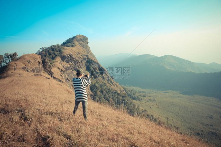 年轻女人站在岩石高山顶上拍照图片