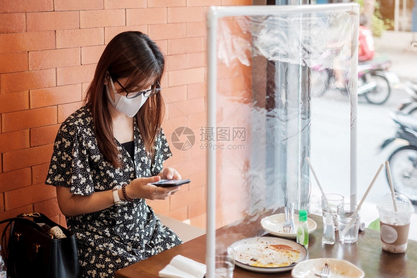 人们分离亚洲妇女在餐厅饮期间使用智能手机将防护罩塑料隔开保护共生19年大流行后在社交失常新的正和生活之后的冠状渗透社会偏移的图片