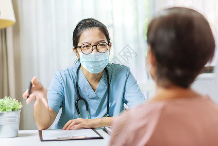 开业在即生活健康身穿蓝色制服和保护面罩的亚洲女医生向院执业师高级女病人提供戴眼镜和外科面具的建议以撰写处方信息的在医院开业师身上戴眼镜和背景