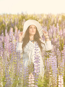 穿着白色帽子和外套夏日草原的时装年轻女子景观化羽扇豆图片