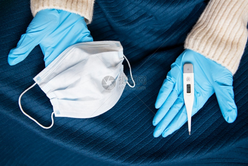 关心发烧成人一个戴乳胶手套的女孩右拿着一个医用口罩左手拿着一个温度计在你面前伸出双臂和流行中的自我控制和的概念一个戴着乳胶手套的图片