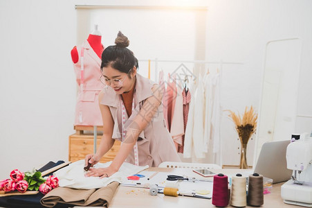 工作室厂在家庭办公室讲习班上工作的有吸引力亚洲时装设计师女时装设计师在家庭办公室工作时尚妇女创造新的布料设计汇编裁缝和纫衣服年轻的高清图片素材