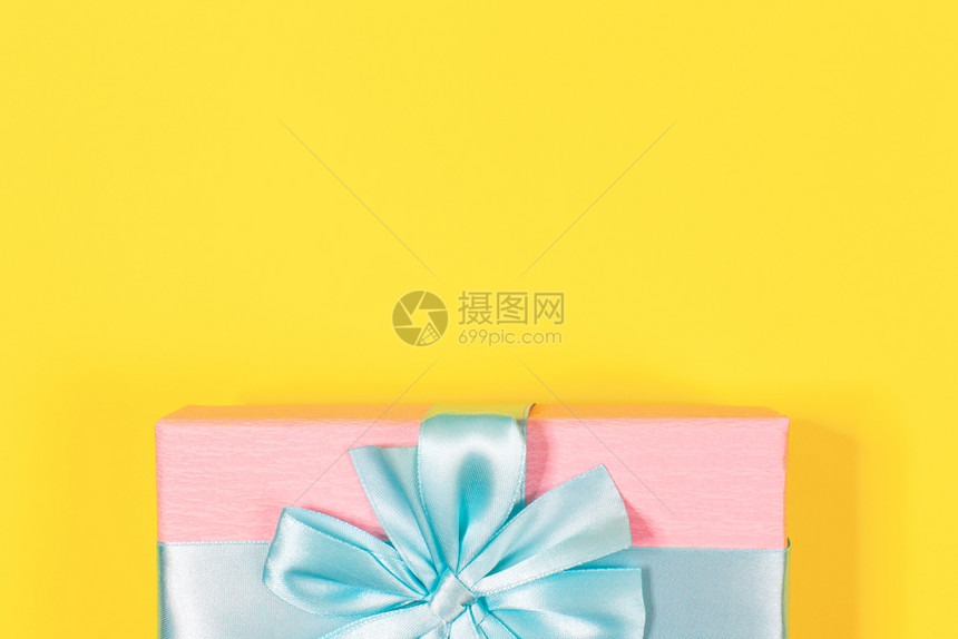 美丽有创造力的粉红礼品盒上面绑着蓝丝带顶端在黄底背景的弓下粉红礼物盒文本复制空间最小平板版面的翻空间生日新年母亲节妇女庆祝活动概图片
