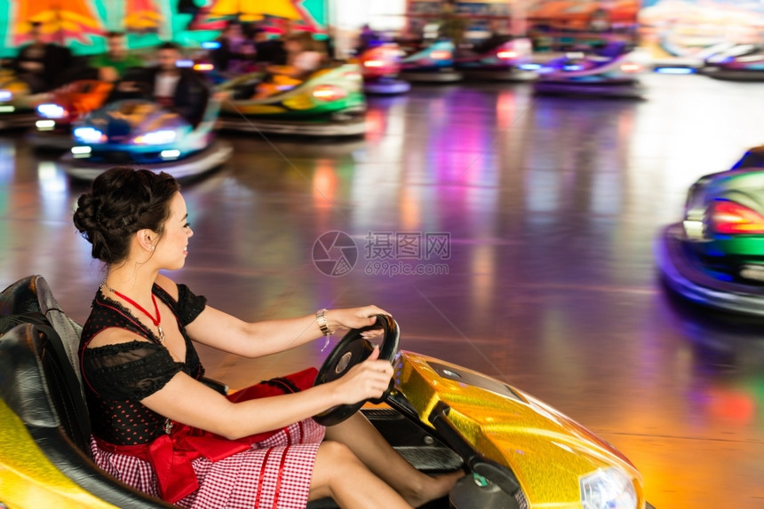 高德纳女在娱乐公园的一辆电动面包车中一个美丽的女孩穿着典型德国Dirndl服装在游乐园的一辆电动保险车中背景美丽女孩身穿彩色和灯图片