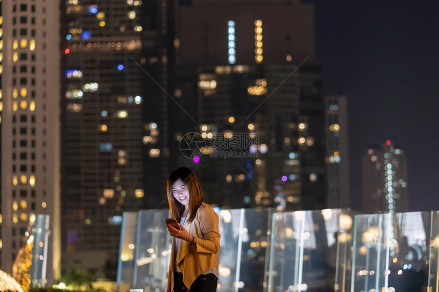 快乐的使用智能手机亚洲女商人在泰国Bangkok河边金融区地使用带微笑动作的智能移电话具有职业概念的技术在Technologyw图片