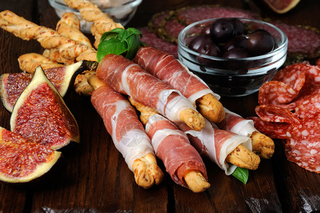帕尔马干酪花絮火腿安提帕斯托零食的Dish面包棒用香肠和橄榄包裹在木质表面的上背景图片