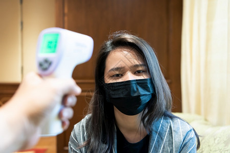 使用电子测温枪给佩戴口罩的女患者测量体温图片