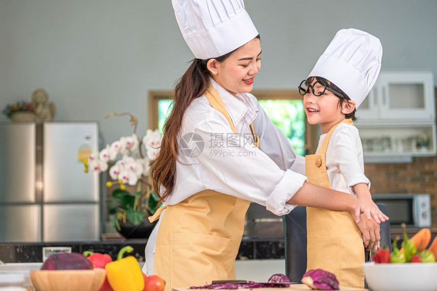 为了帮助快乐的亚洲美女打扮漂亮可爱的小男孩厨师服装准备在家中厨房做饭人们的生活方式和家庭自制食物原料概念两个泰国人的生活2个泰国图片