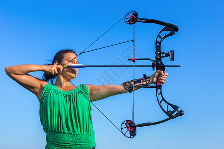 弓箭射击女士夏天德尔登年轻黑头发的哥伦布女人在蓝天向弓箭瞄准背景
