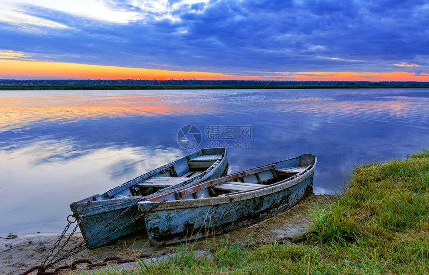 金的自然两条旧蓝绿色木制船在清晨宁静的河岸上链紧锁一条平静的河流太阳升起的光芒照亮了宽阔河流海岸的夏季风景两艘旧的蓝色绿船只被金图片