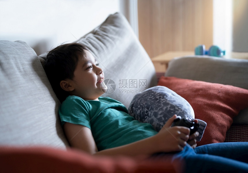 兴奋的在家玩网上游戏年轻男孩坐在沙发上玩具乐周末放轻松新生活方式与相伴后的习惯笑声iwhitbox可爱的亚洲人图片