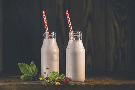 木制的冰沙装有美味草莓奶昔或溜冰瓶在黑木桌和背景上放着野草莓枝新鲜图片