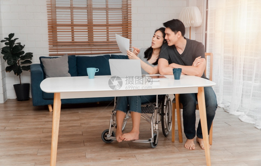 在室内鼓励车祸后坐在轮椅上的妇女在家中与她的爱人一起使用计算机工作相互照顾的概念和新技术使残疾人在社会中享有平等地位一社会中的平图片