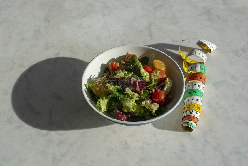 混合绿色和紫沙拉与白大理石桌子上的测量带节食健身康概念背景与复制空间的阴影混合绿色和紫沙拉与测量带莴苣仪表番茄图片