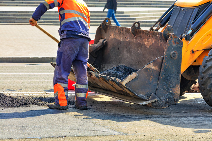 水平的人们道路维修技术员在公路建设期间从一桶推土机上用新鲜沥青浇灌一桶马路推土机修补沥青路部分一名工人将新鲜沥青倒到路的贫乏部分图片