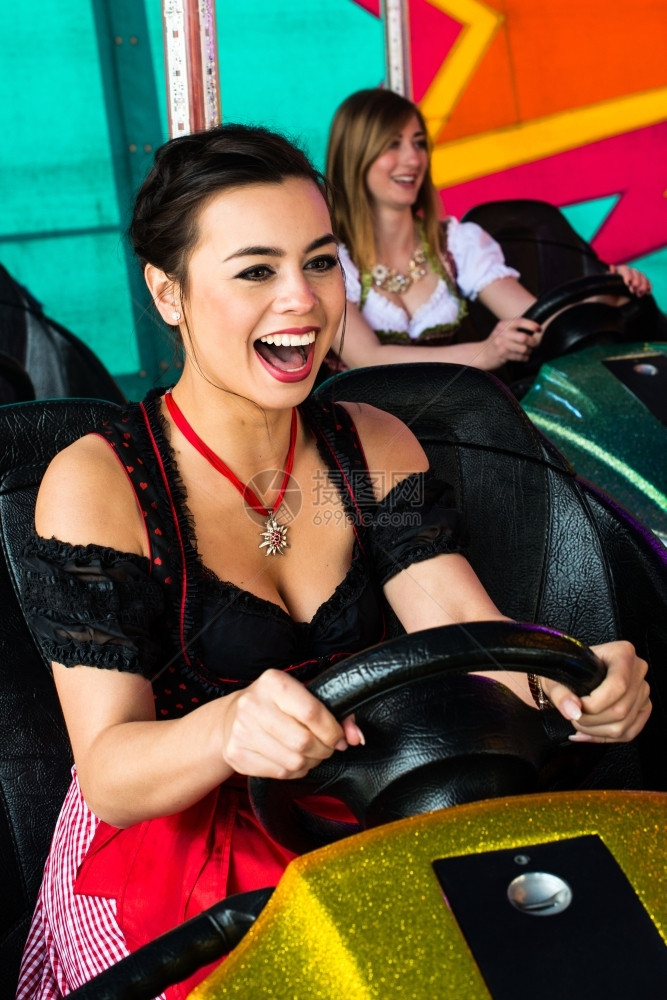 女孩们典型的享受在娱乐公园的一辆电动保险杠车中穿着典型德国Dirndl服装背景彩色和灯光明亮的美丽女孩在娱乐公园的一辆电动保险面图片