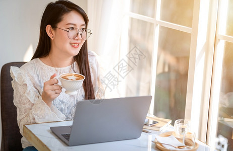 女孩背景商用白色的马克杯吸引人女商用笔记本电脑和咖啡店智能手机商业生活方式交流概念与笔记本电脑和智能手机一起工作的零用笔记本散工背景