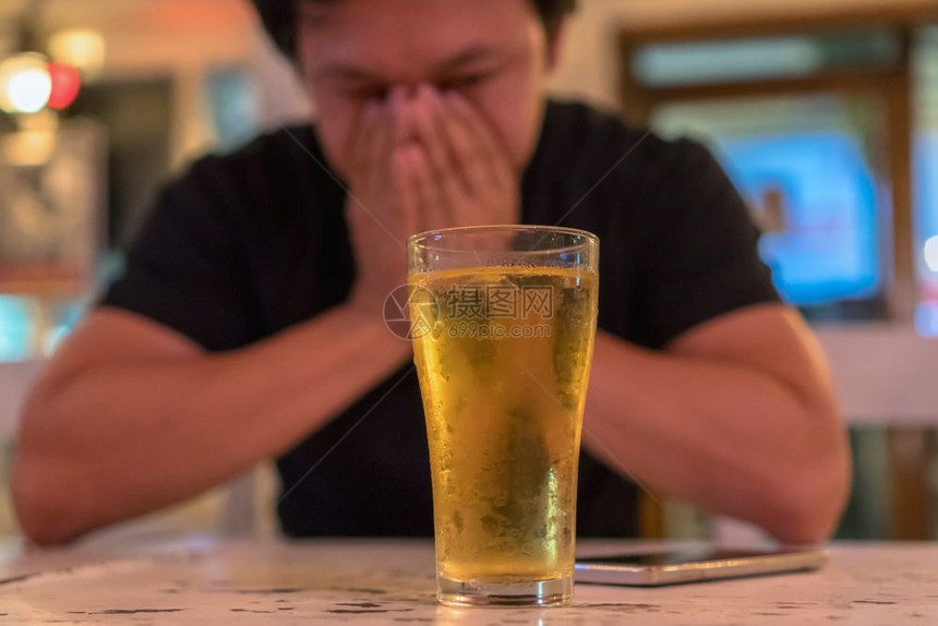 庆典咖啡店在室内亚洲青年男子在孤单和沮丧的动作中手握着面部看到酒厅和餐馆有一杯啤酒低光忧郁和饮酒概念图片