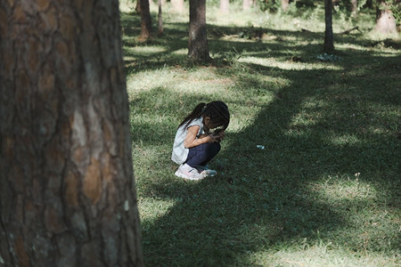 小女孩坐在草地上闭着眼睛在公园里玩捉迷藏图片