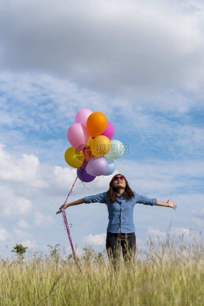 女人拿着气球在绿色草地白云和蓝天空上奔跑快乐轻松的天空手拿着充满活力的空气球在生日派对上欢快的盛宴玩优质白色夏天图片
